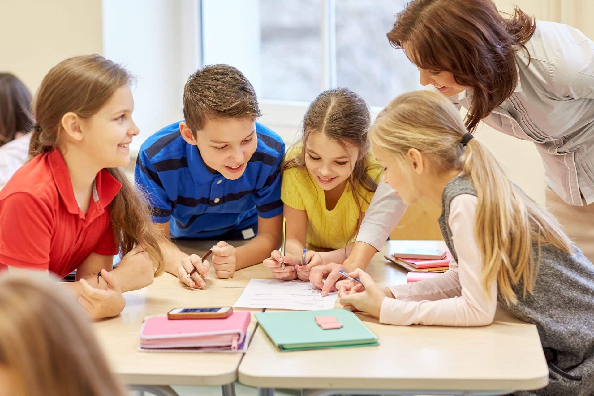 Gruppo di quattro studenti, che svolgono insieme un'attività di classe, affiancati da un'insegnante